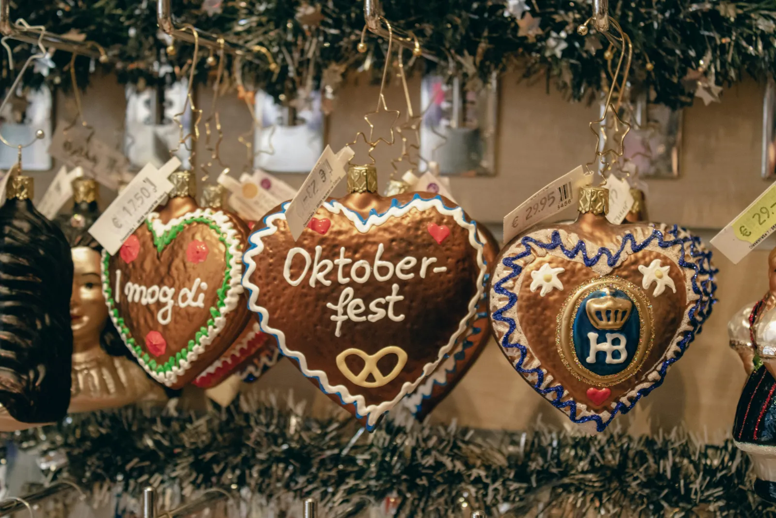 Julgranskulor av glas formade som pepparkakshjärtan. På det mittersta står det “Oktoberfest” ovanför en kringla.