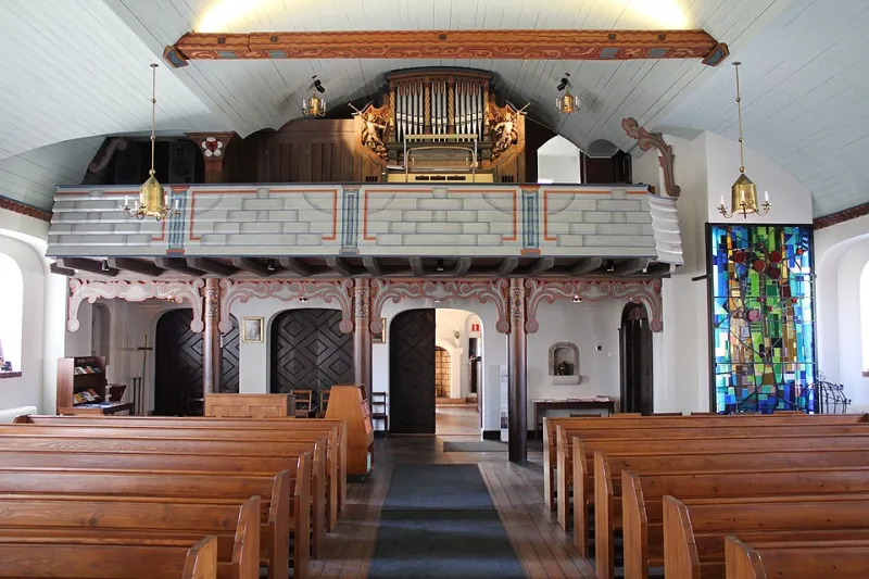 Orgeln på läktaren i Enskede kyrka, med silverfärgade pipor mellan vridna pelare och en förgylld ängel med basun på var sida.