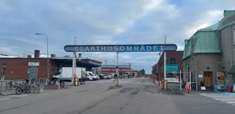 Infart med bommar under en stor skylt med texten Slakthusområdet. Till höger ett tegelhus med grönt tak